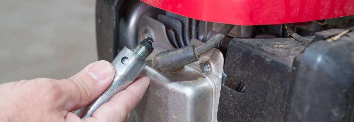 Hand hält Zündkerze an Rasenmäher